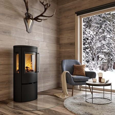 Moderne woonkamer met zwarte houtkachel naast fauteuil en winterlandschap buiten, passend bij houtkachel onderdelen en onderhoud